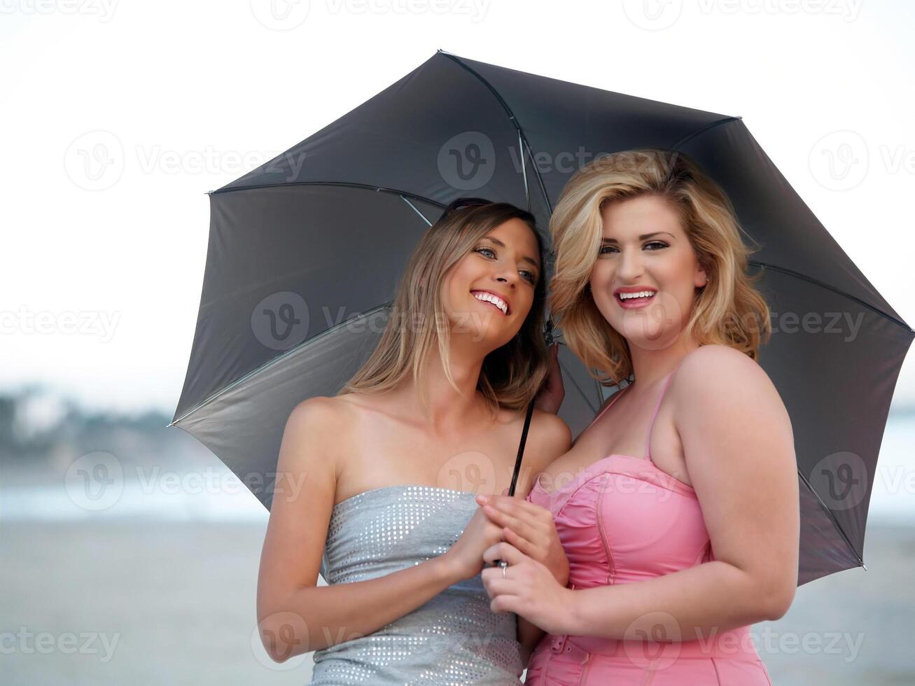 två ung kvinnor på strand innehav paraply foto