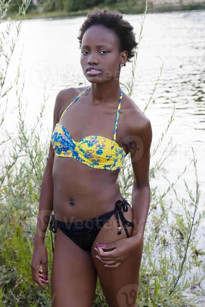 mager svart tonåring flicka badning kostym förbi flod foto