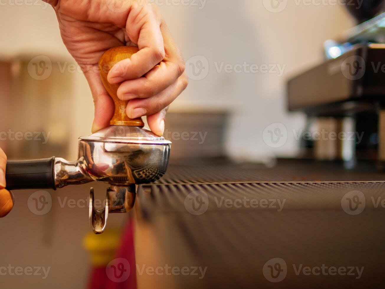 hand av en Barista innehav en portafilter och en kaffe manipulera framställning ett espresso kaffe. Barista trycker på jord kaffe använder sig av en manipulera i en kaffe affär foto