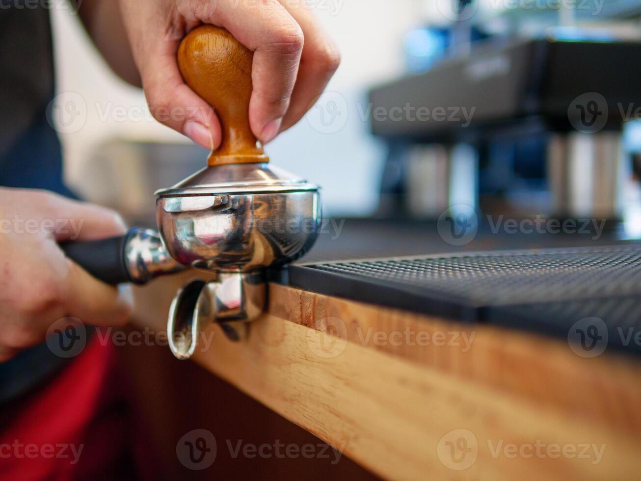 hand av en Barista innehav en portafilter och en kaffe manipulera framställning ett espresso kaffe. Barista trycker på jord kaffe använder sig av en manipulera i en kaffe affär foto