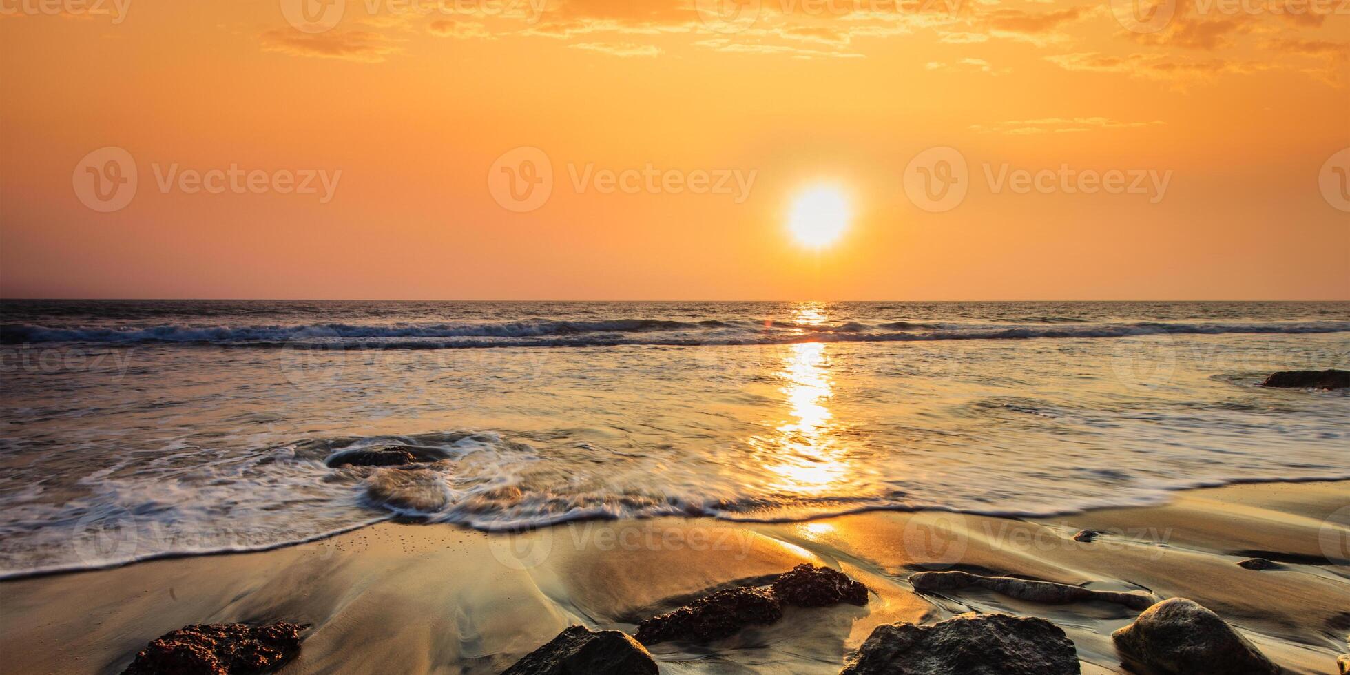 vågor och stenar på solnedgångens strand foto