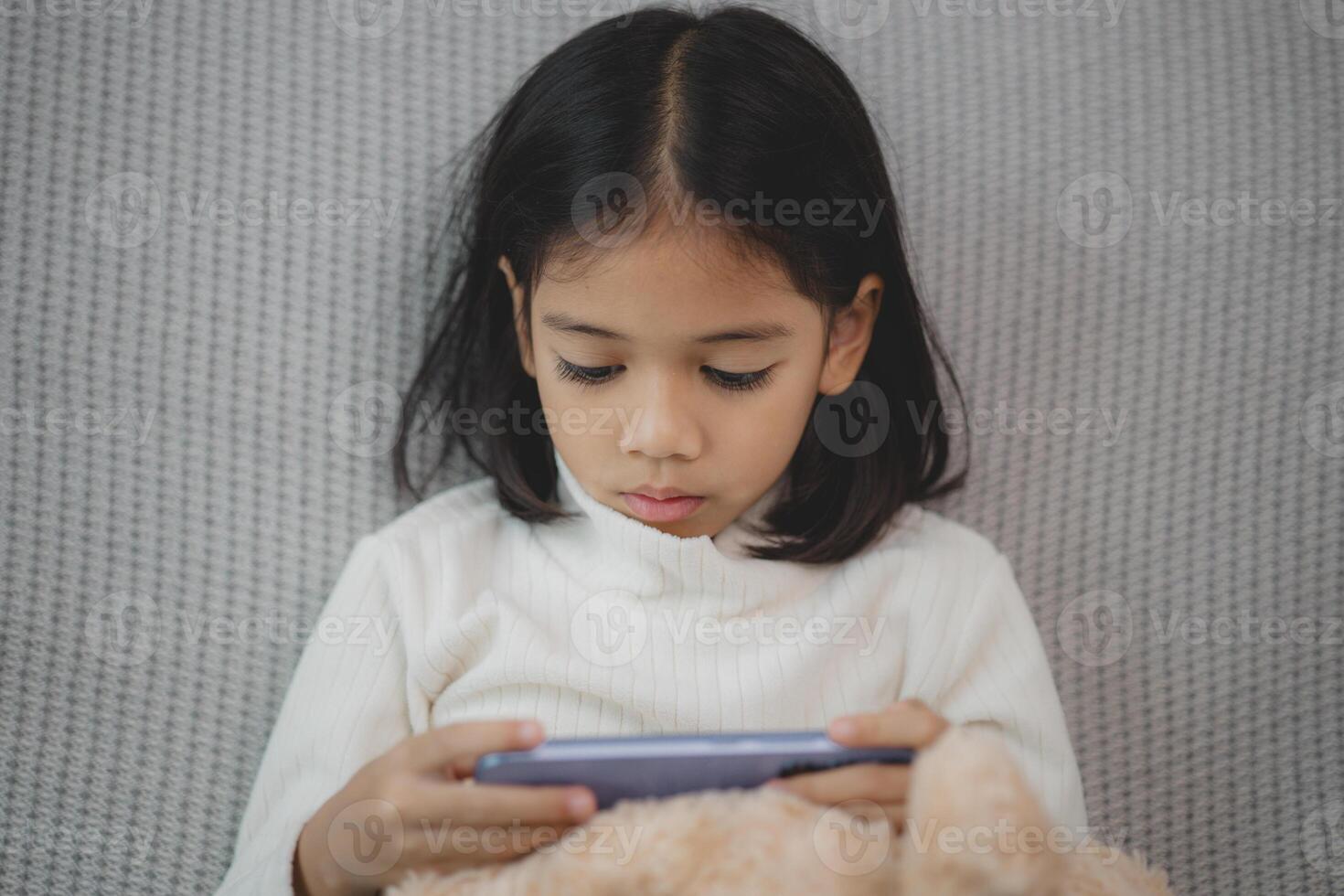 en ung flicka är spelar en video spel på en läsplatta medan Sammanträde på en säng foto