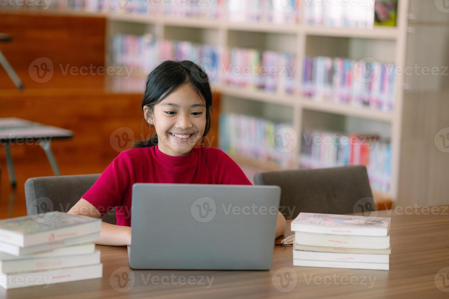 en ung flicka är Sammanträde på en tabell med en bärbar dator och en stack av böcker foto