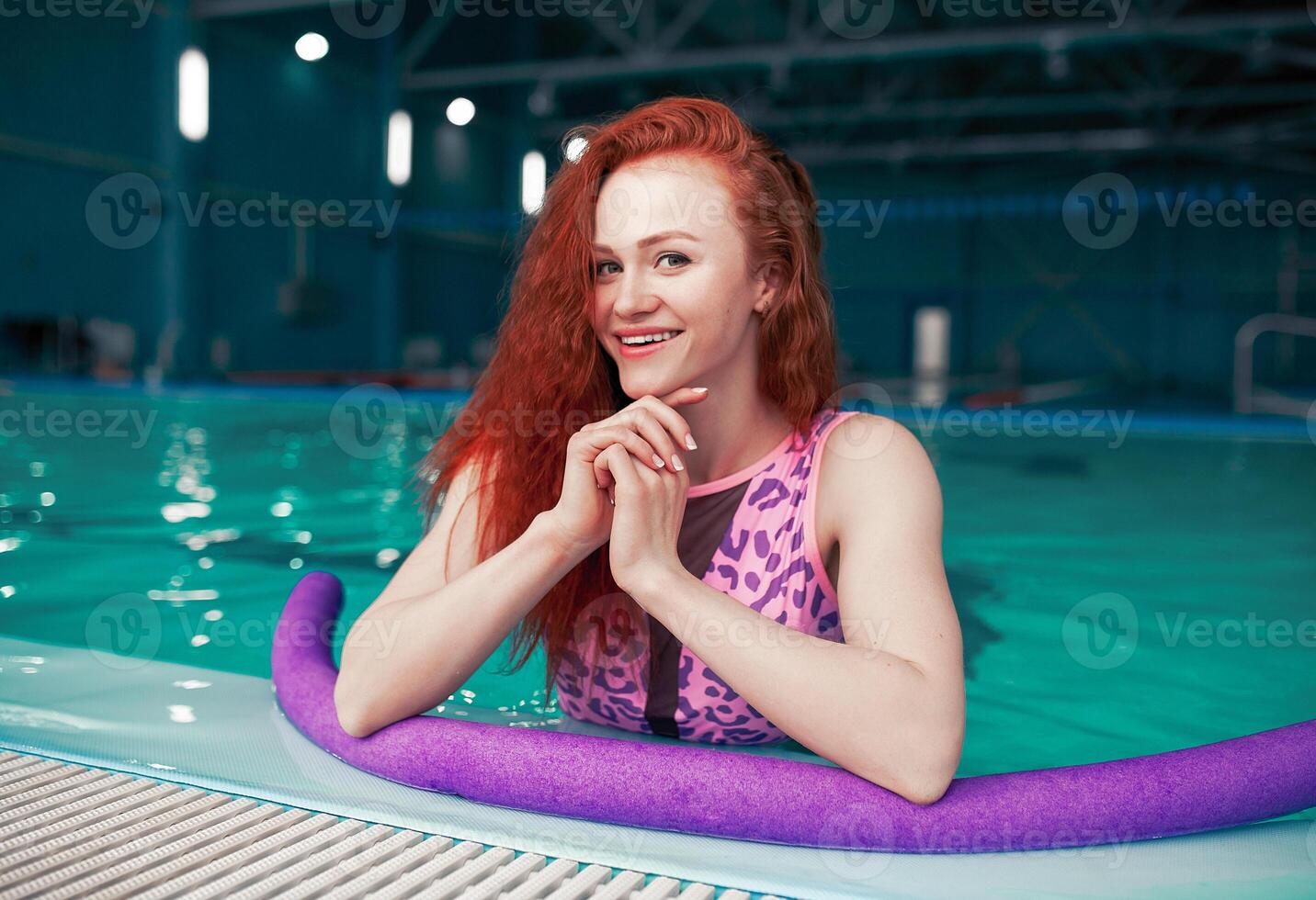 skön ung rödhårig flicka i en modern baddräkt i de stil av de 80s står med de spaghetti i henne händer i de inomhus- simning slå samman foto