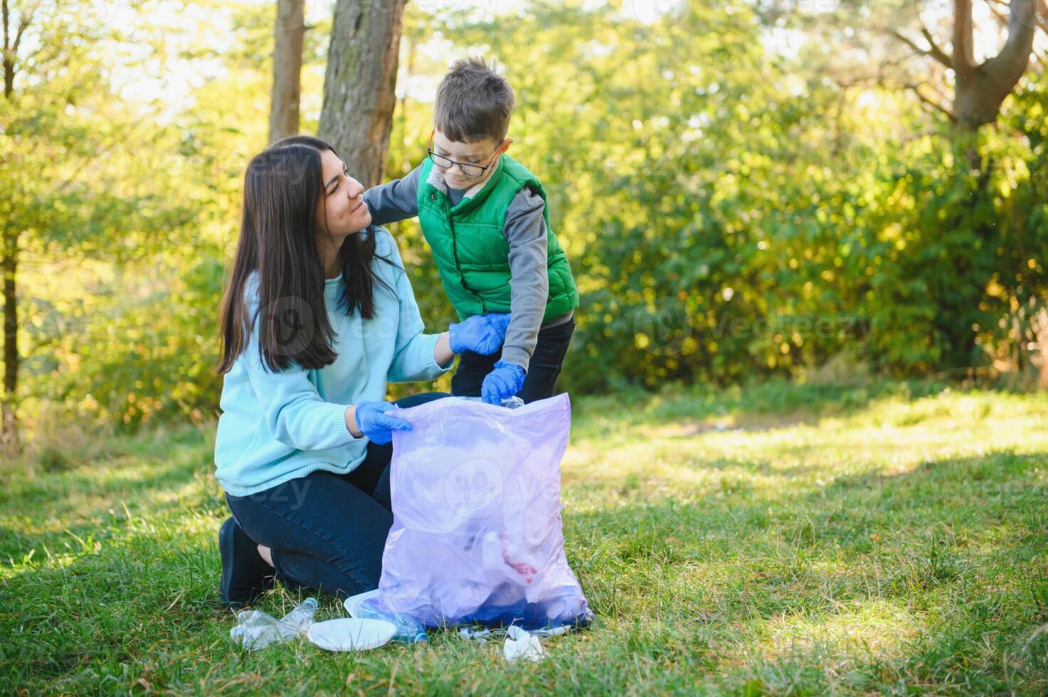 kvinna volontär- och liten pojke plockning upp de plast sopor och sätta den i biologiskt nedbrytbar soppåse utomhus. ekologi, återvinning och skydd av natur begrepp. miljö- skydd. foto