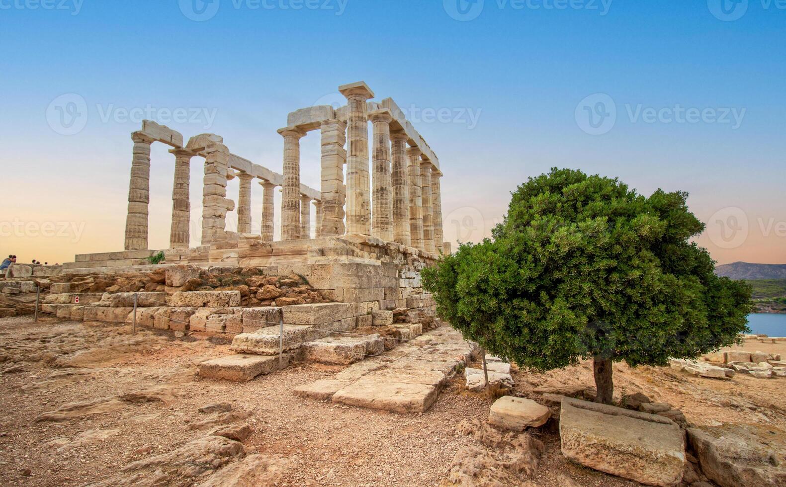 de känd tempel av poseidon i grekland med en grön träd på solnedgång. i grekisk mytologi, de Gud av de hav. cape sounion, ruiner av de gammal tempel med blå himmel foto