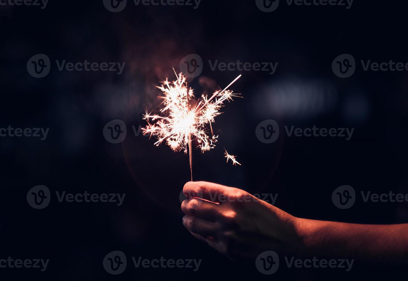 hand som håller brinnande tomtebloss blast på en svart bakgrund på natten, semester fest foto