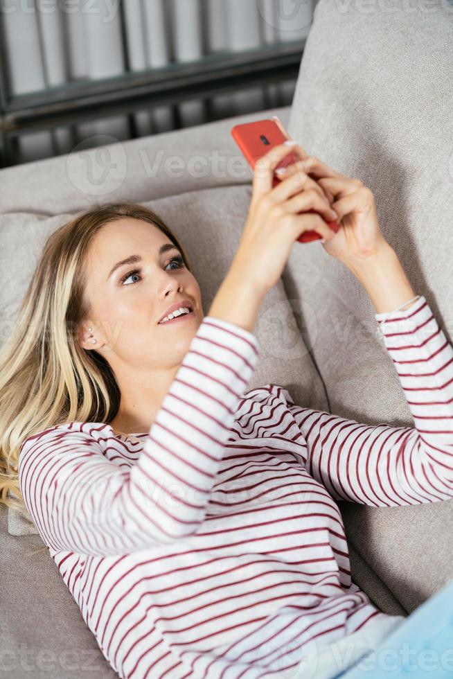 leende kvinna med sin smartphone liggande på soffan. foto