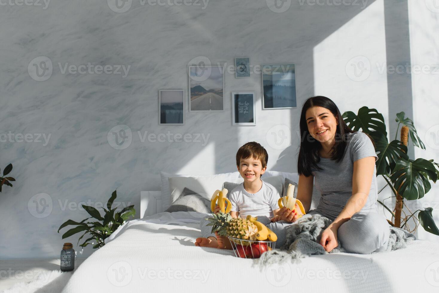 mamma med son i pyjamas äter frukt på säng. porträtt Lycklig, leende, glad familj, moden och son har frukost i säng, överraskning på mamma dag. positiv mänsklig känslor foto