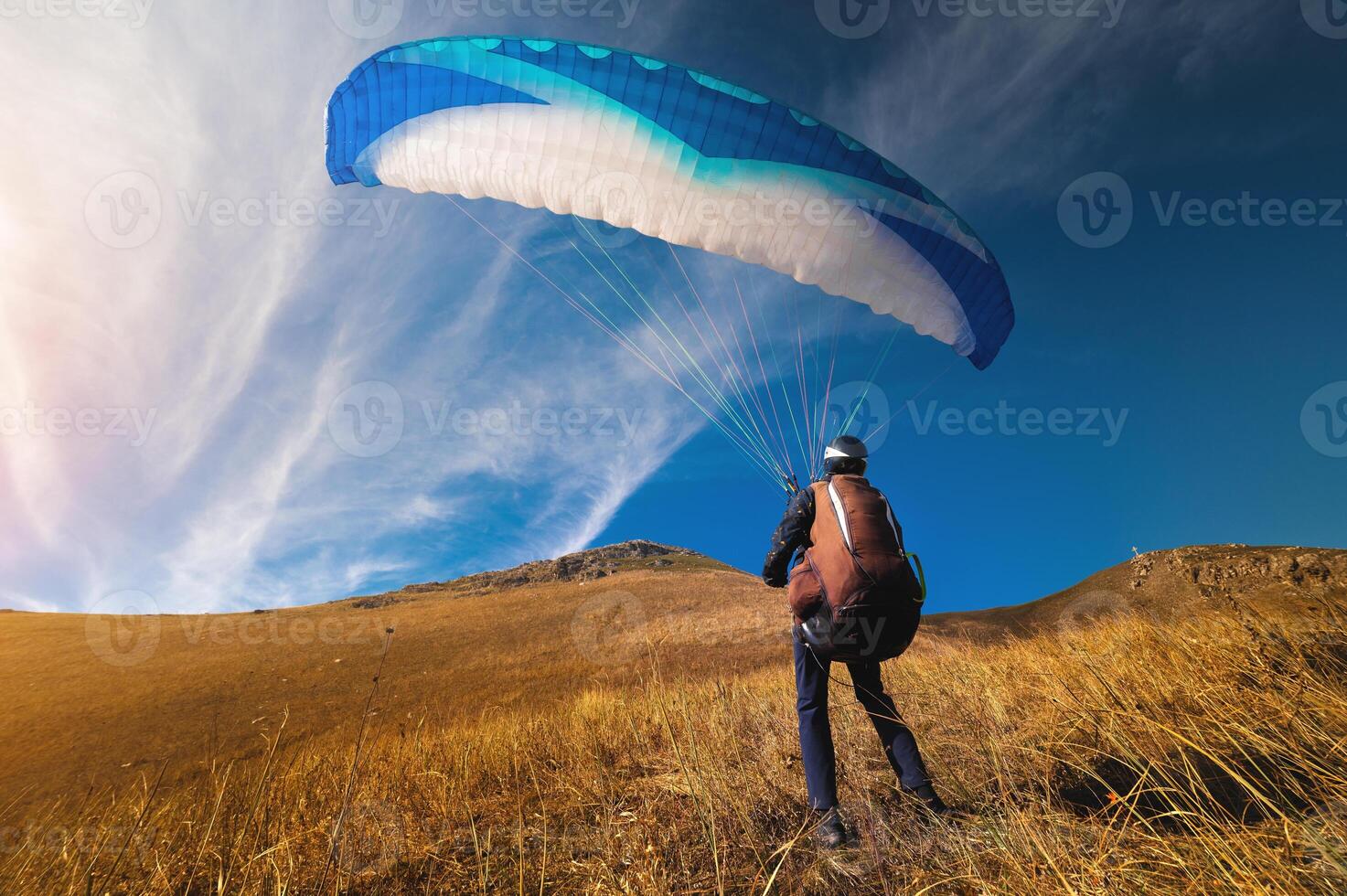 paraglider står på gul gräs i en fält och innehar hans fallskärm i de luft. extrem sport foto