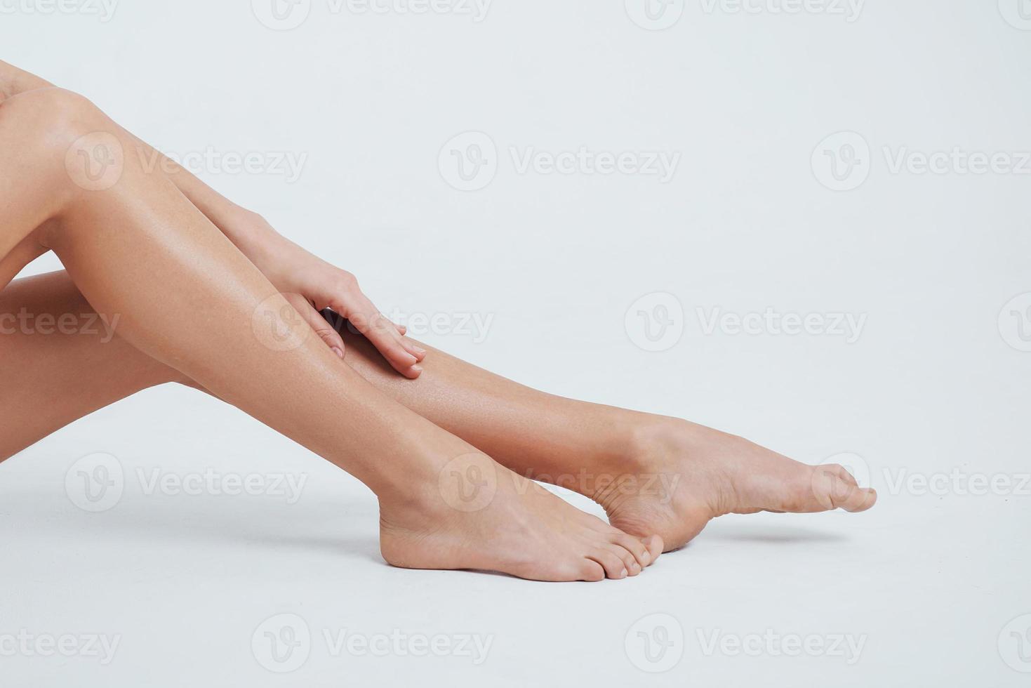 närbild foto av kvinnliga släta ben med handen på den och vit bakgrund bakom