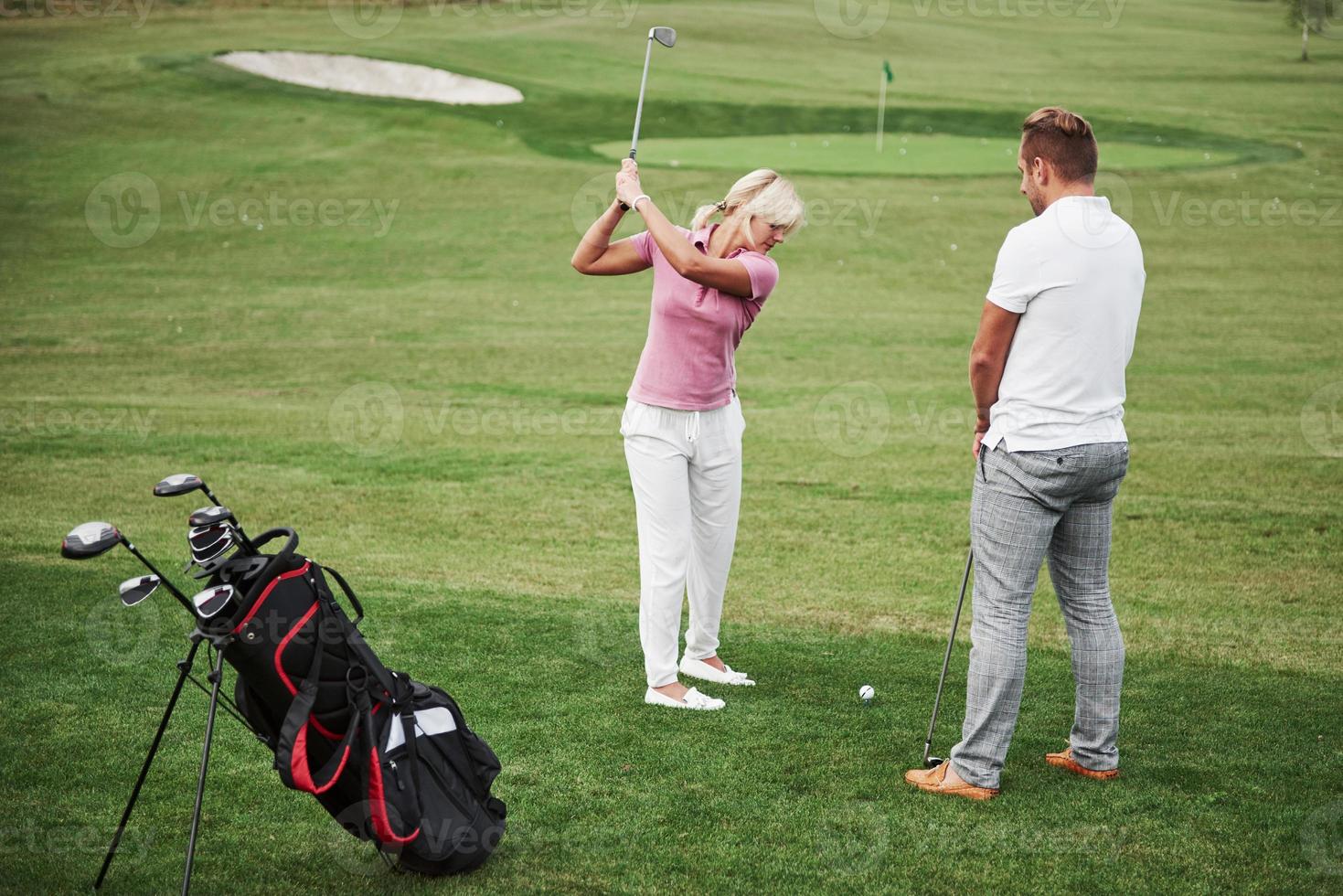 flicka spelar golf och slå av putter på green. hennes lärare hjälper till att utforska tekniken och göra sina första slag foto