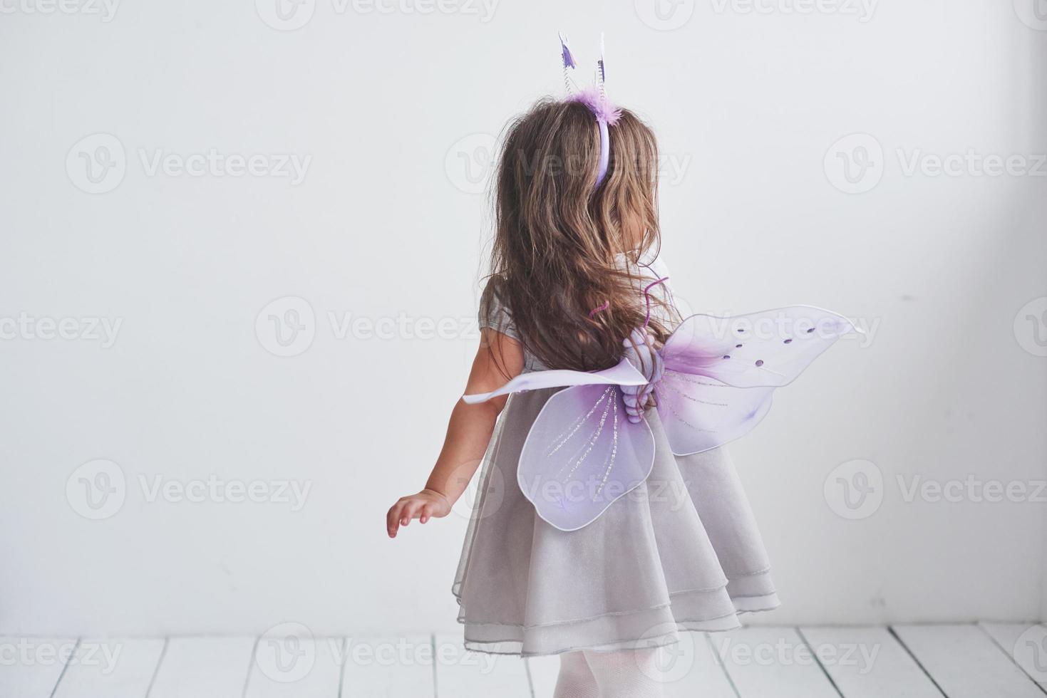 visa dina vingar. härlig liten flicka i älva kostymen står i rum med vit bakgrund foto