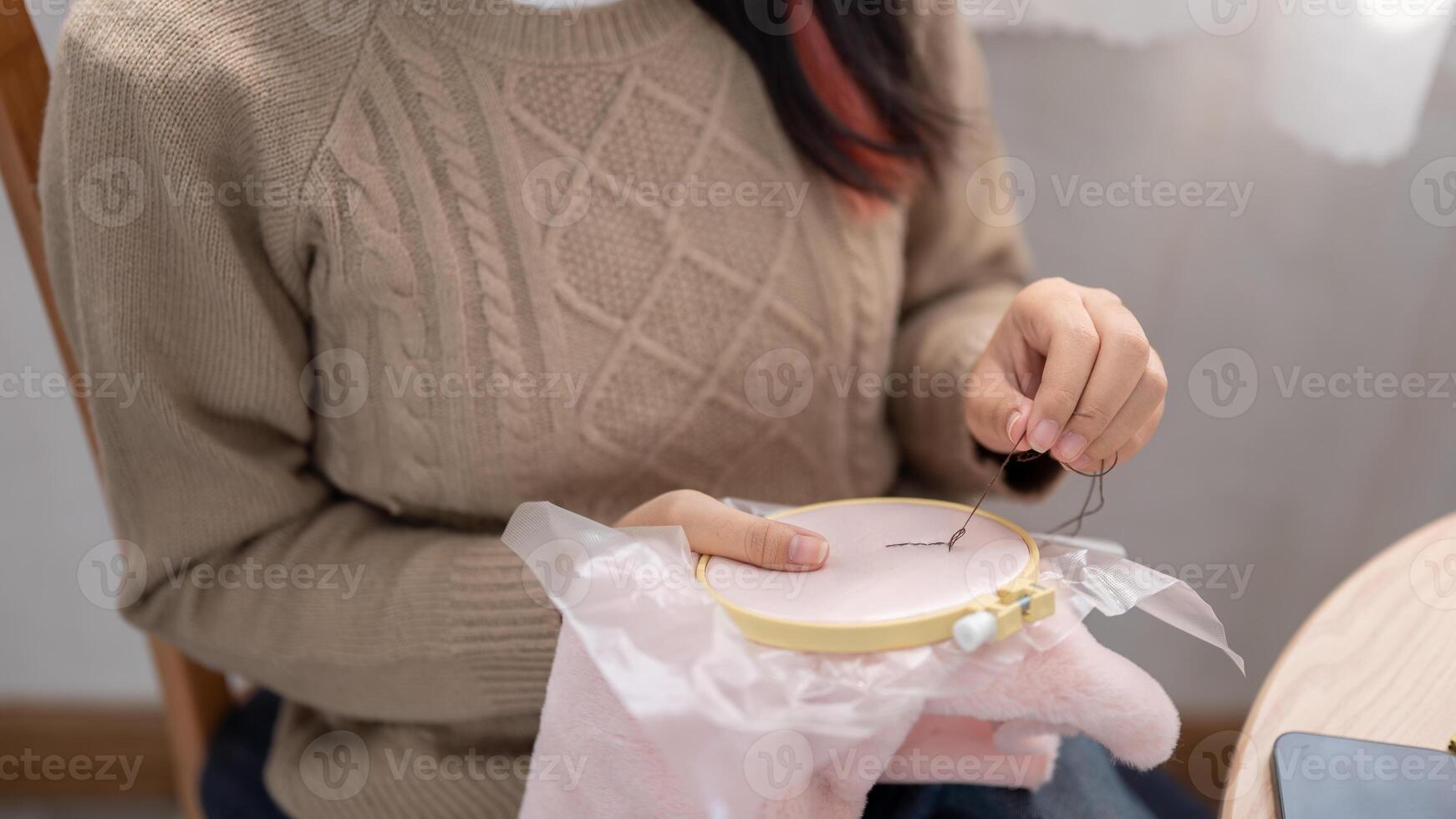 en kvinna är handsömnad en mönster på ett broderi ram, njuter henne hobby på Hem. foto