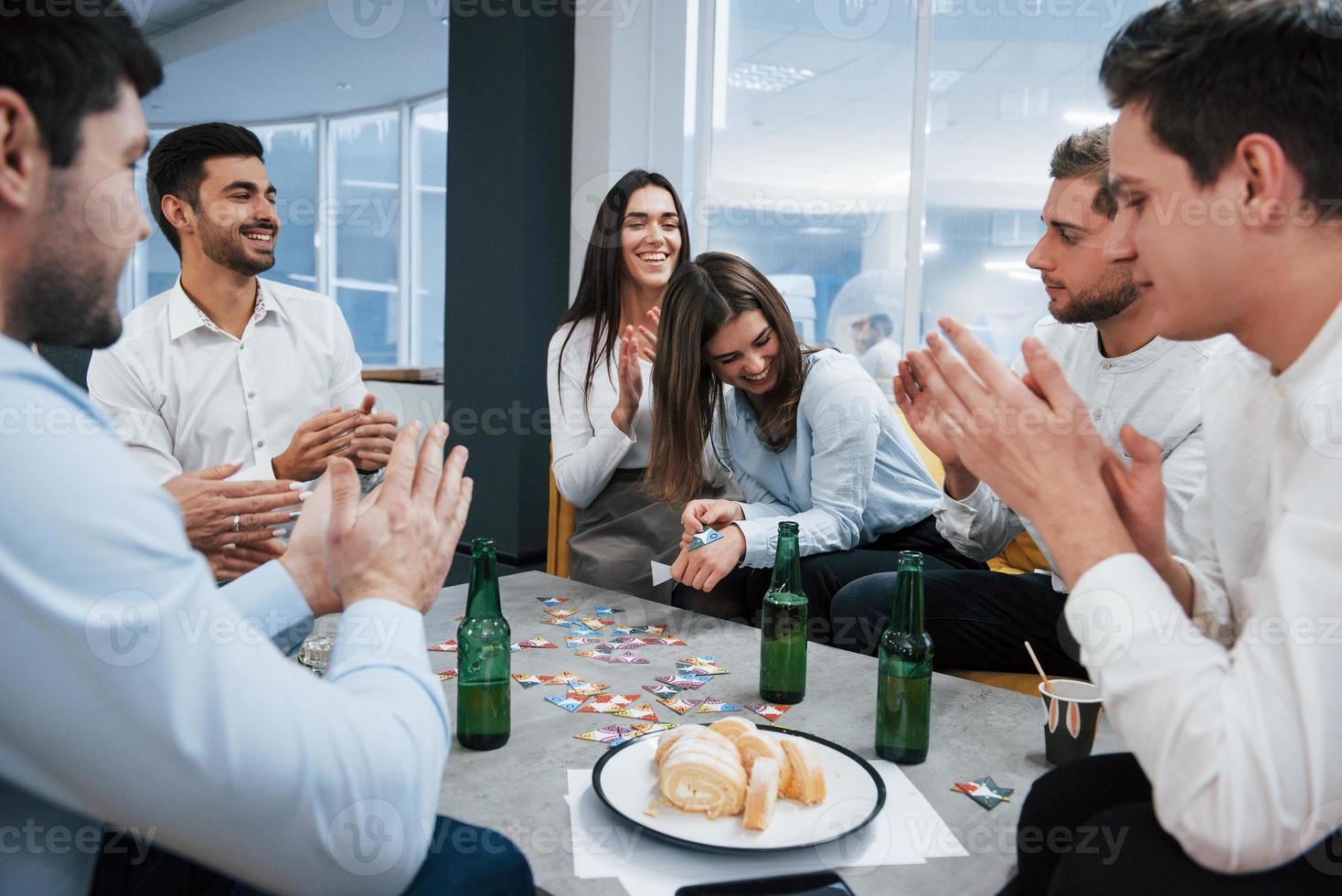 bra skämt. firar framgångsrik affär. unga kontorsanställda som sitter nära bordet med alkohol foto
