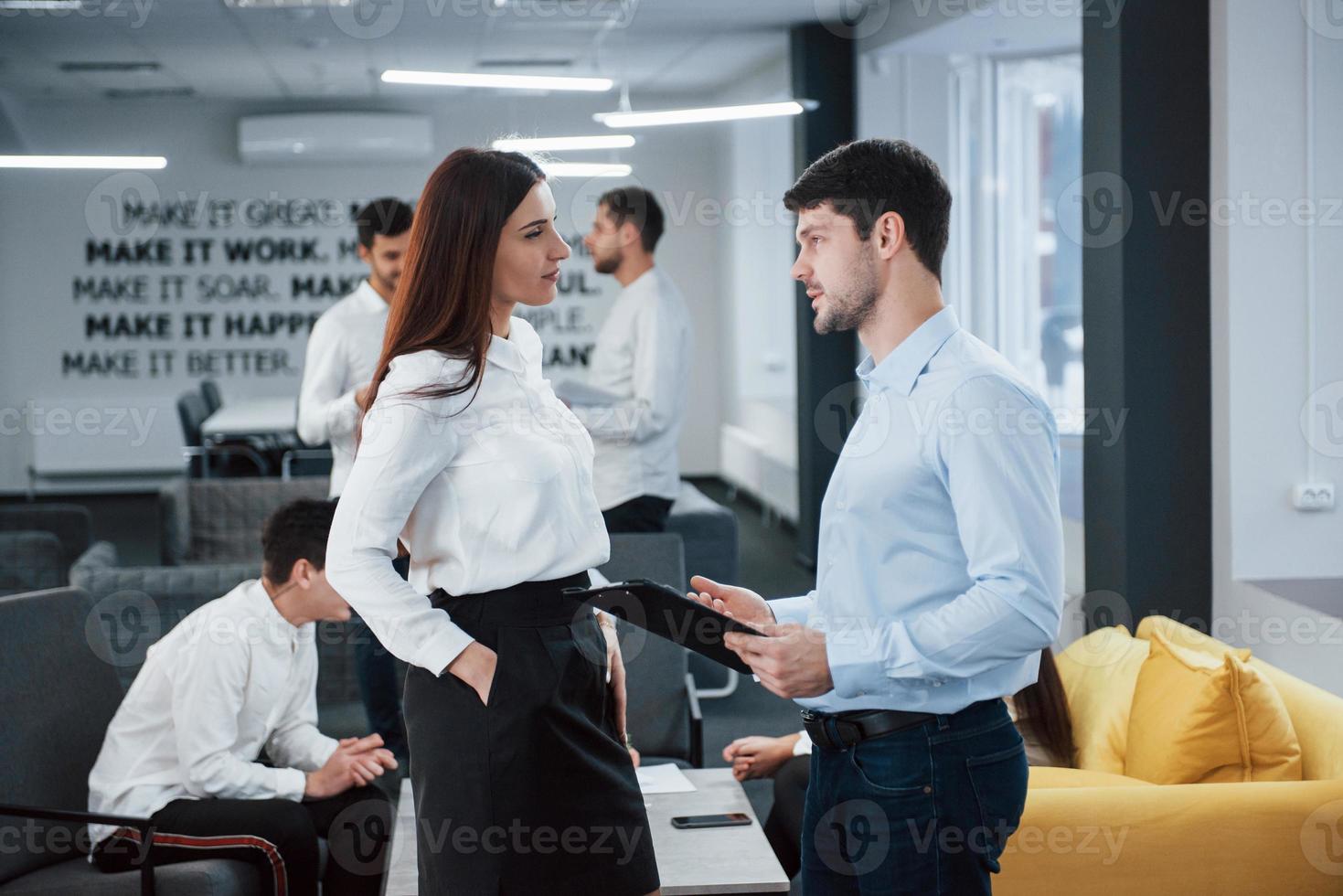två kontorsarbetare i klassiska kläder som pratar inför anställda foto