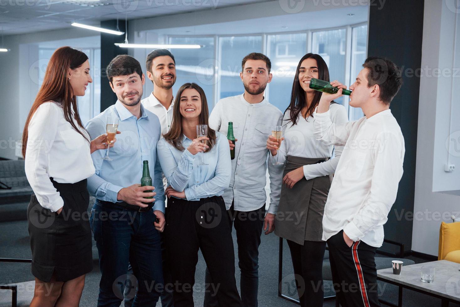 vila tillsammans efter jobbet. foto av ungt team i klassiska kläder som håller drinkar i det moderna bra upplysta kontoret