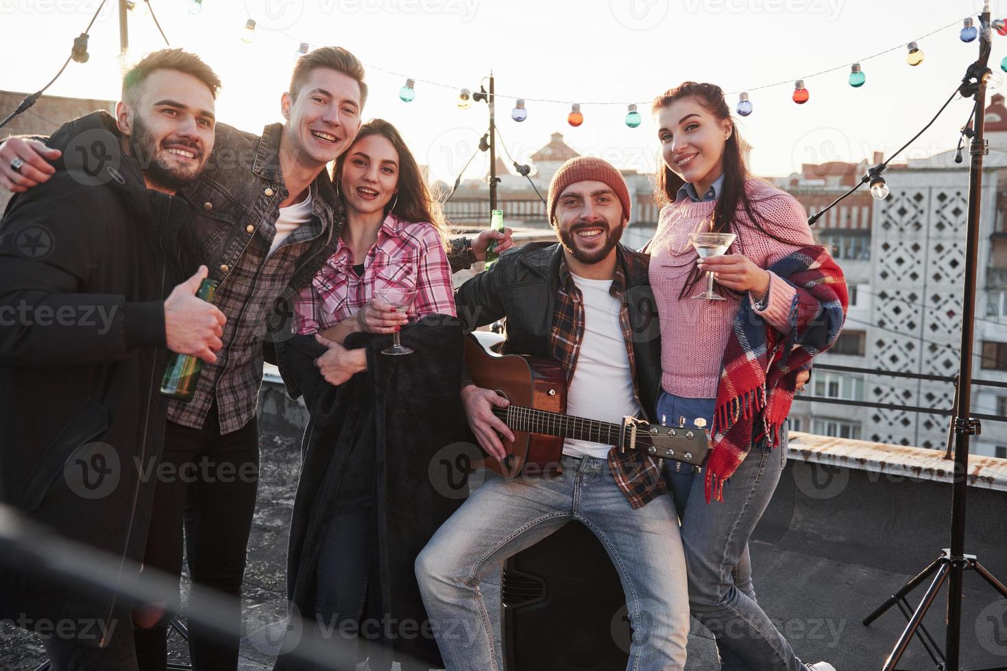 fantastiskt humör. fest på taket. fem snygga vänner som poserar på bilden med alkohol och gitarr foto