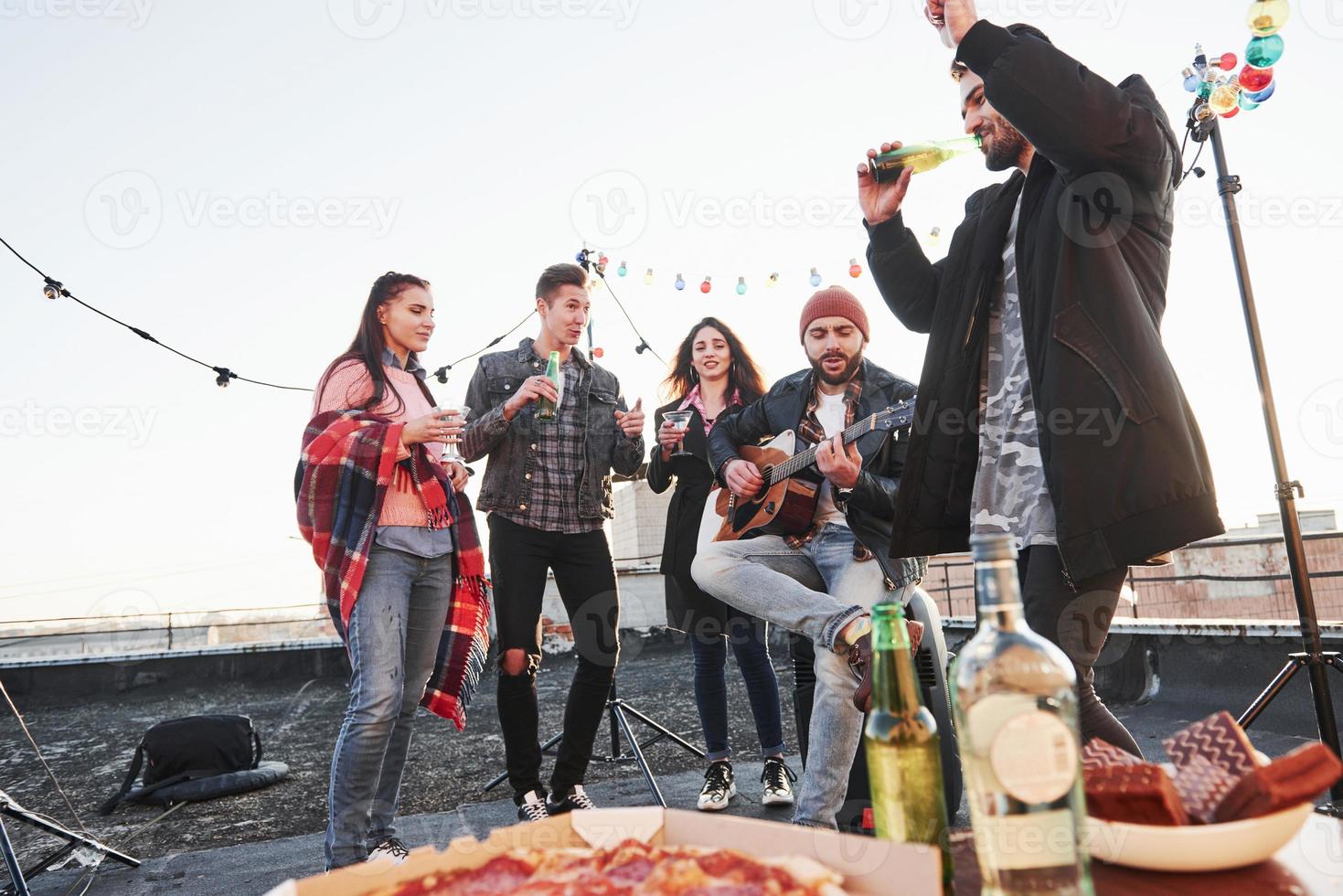 njuter av låten. bord med mat. helg på taket med gitarr, alkohol och pizza foto