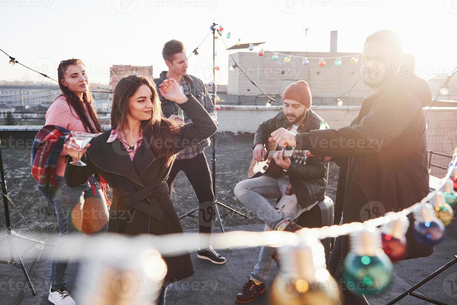 njuter av det senaste varma solljuset. glödlampor runt om på taket där ett ungt gäng vänner har bestämt att spendera sin helg med gitarr och alkohol foto