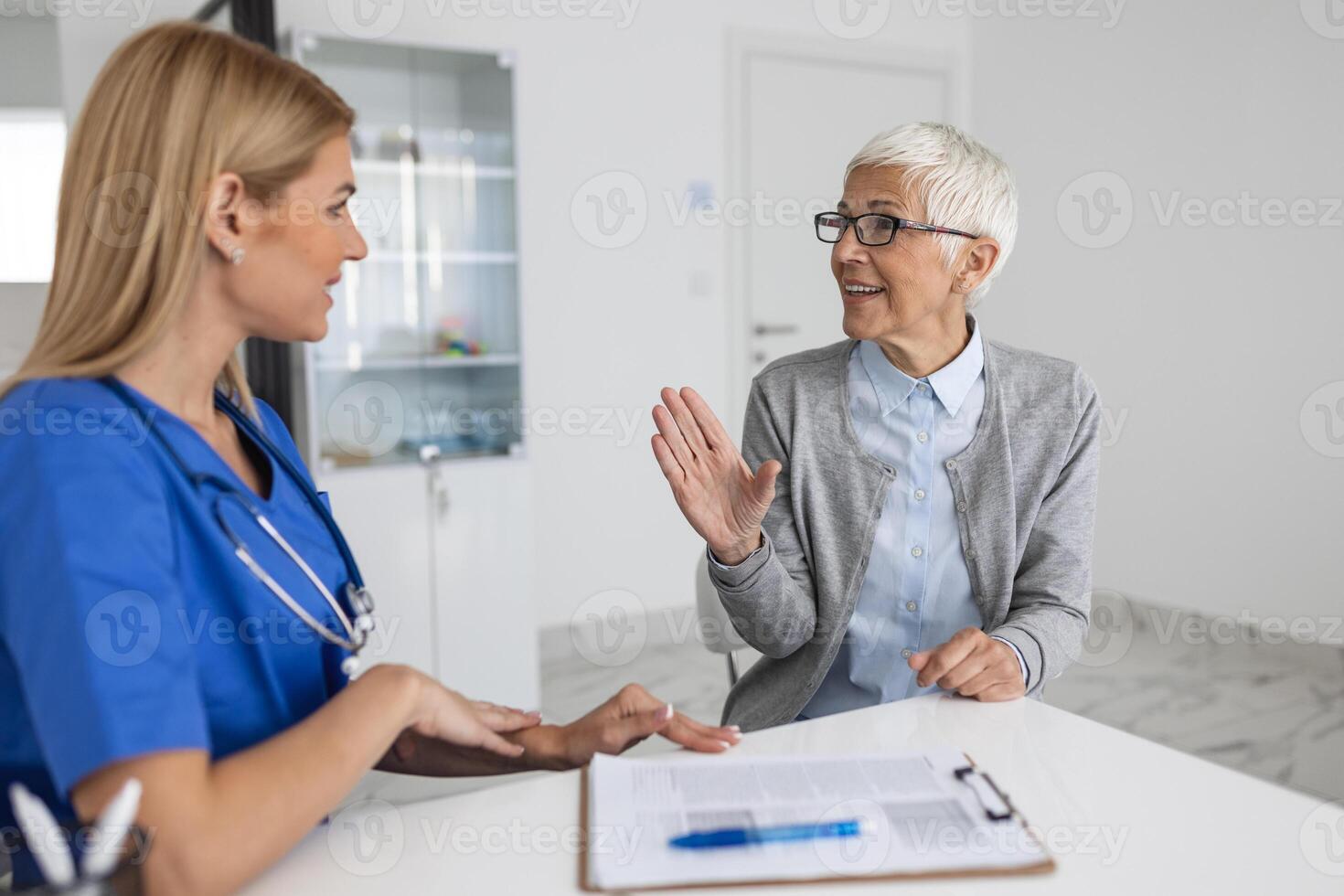 ung kvinna läkare eller gp i vit medicinsk enhetlig rådfråga senior kvinna patient i privat sjukhus. kvinna terapeut tala prata med kvinna klient på samråd i klinik. foto