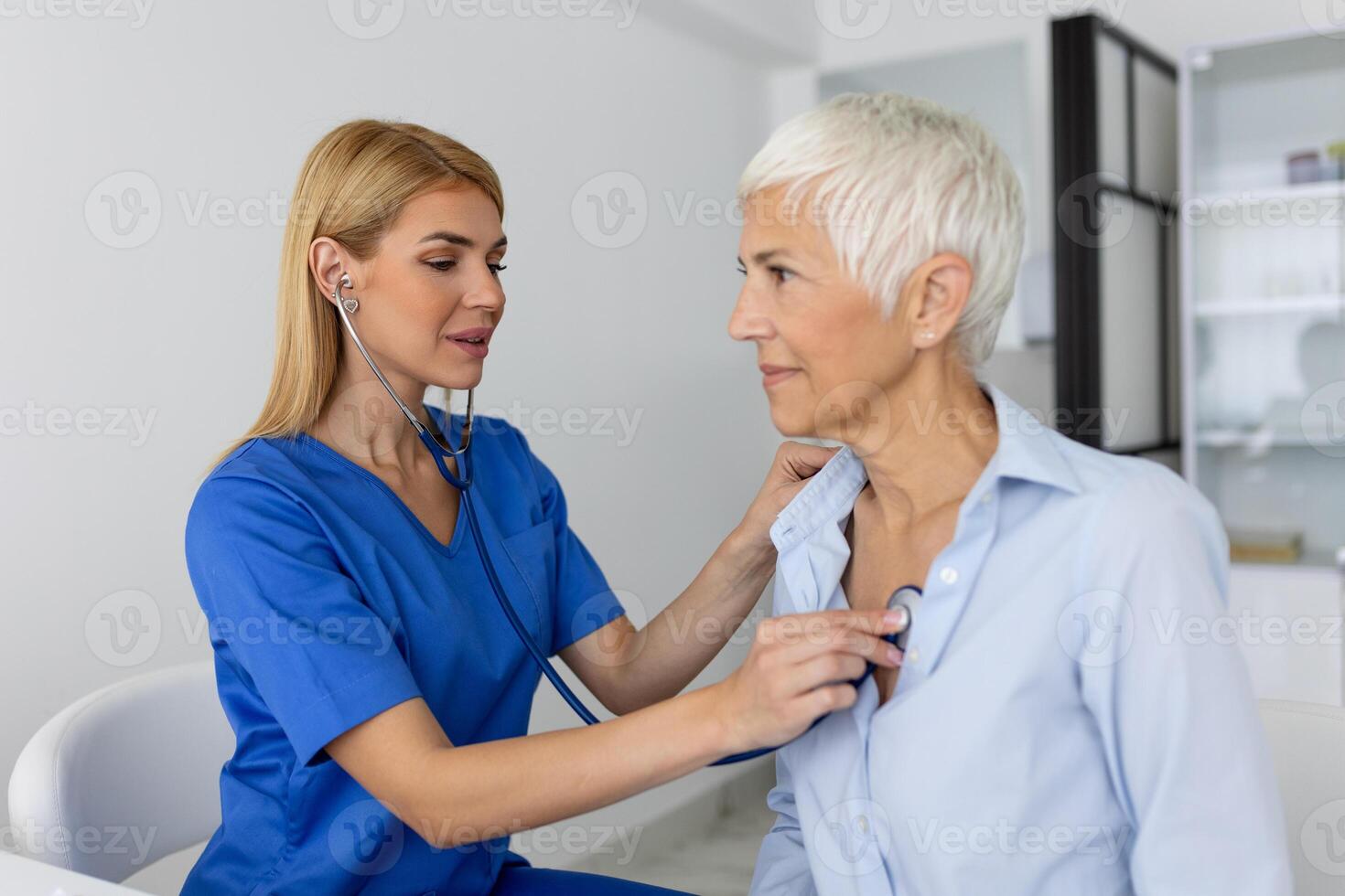 ung kvinna läkare lyssna till senior patient hjärta bröst med stetoskop på klinik möte. kvinna gp kolla upp undersöka kvinna klient med telefonndoskop. sjukvård begrepp. foto