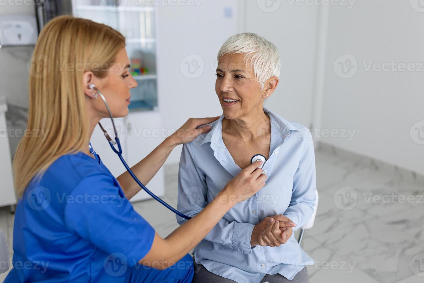 ung kvinna läkare lyssna till senior patient hjärta bröst med stetoskop på klinik möte. kvinna gp kolla upp undersöka kvinna klient med telefonndoskop. sjukvård begrepp. foto