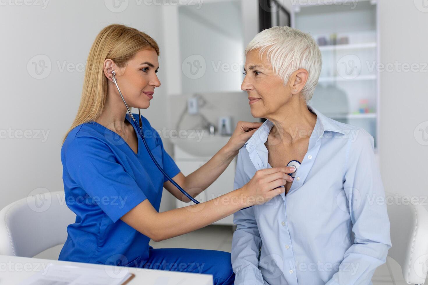 ung kvinna läkare lyssna till senior patient hjärta bröst med stetoskop på klinik möte. kvinna gp kolla upp undersöka kvinna klient med telefonndoskop. sjukvård begrepp. foto