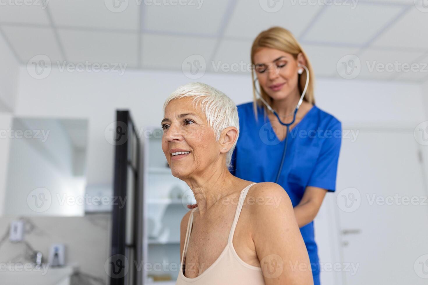 ung kvinna läkare lyssna till senior patient hjärta bröst med stetoskop på klinik möte. kvinna gp kolla upp undersöka kvinna klient med telefonndoskop. sjukvård begrepp. foto