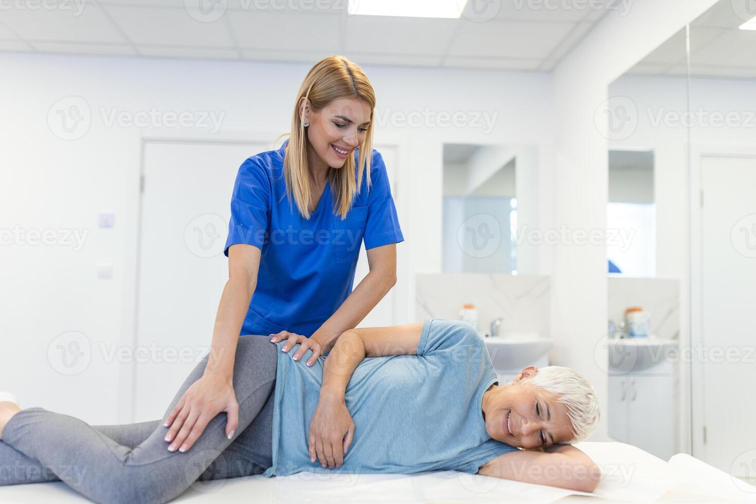 professionell kiropraktor eller fysioterapeut hjälper till läka en senior kvinnas tillbaka. läkare fixar de patient liggande på en soffa av en modern rehabilitering klinik begrepp av fysisk rehabilitering. foto