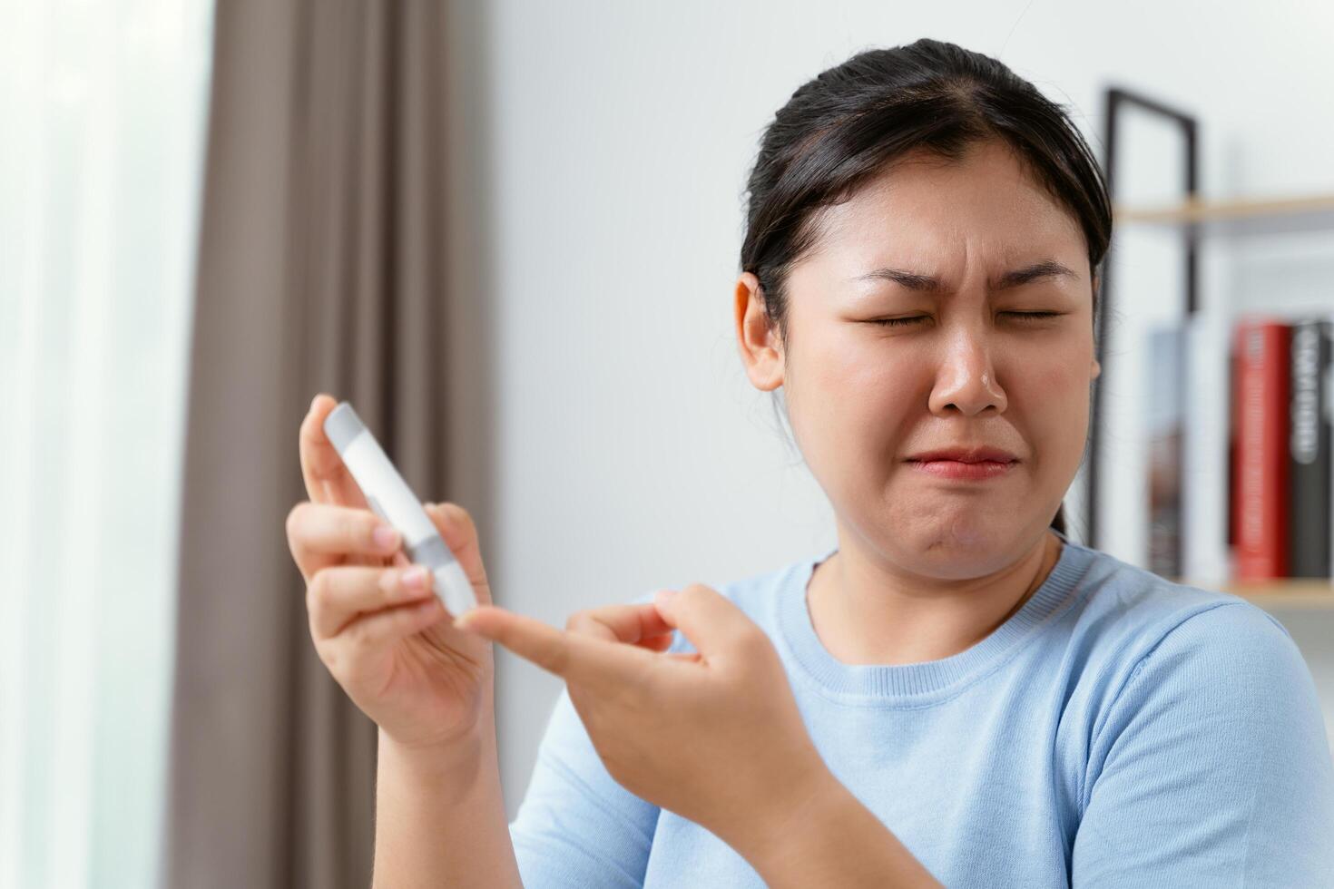 asiatisk kvinna använder sig av lansett på finger för kontroll blod socker nivå förbi glukos meter, diabetes. foto