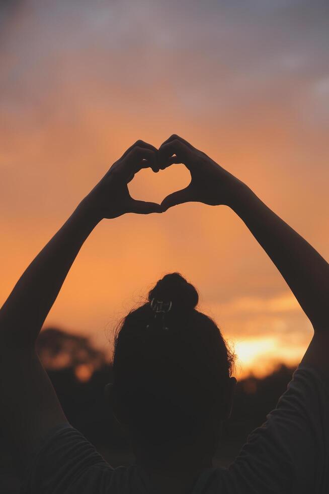 silhuett av händer i hjärta symbol runt om de Sol foto