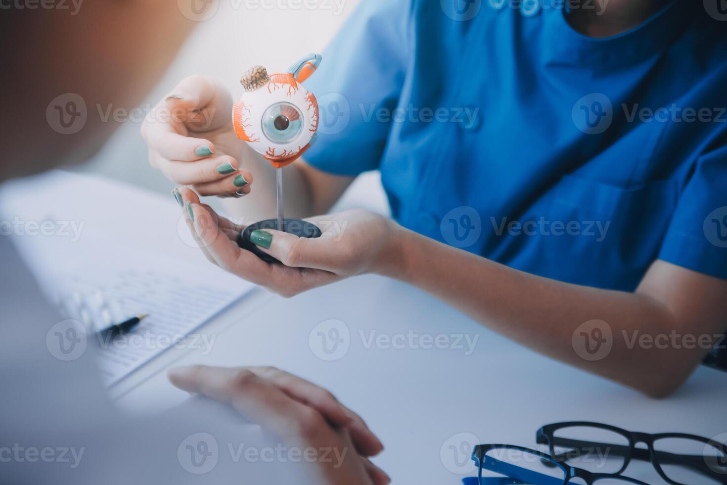 närbild av asiatisk kvinna läkare talande med äldre patient som visar eyeball modell och förklara öga sjukdom i sjukhus foto