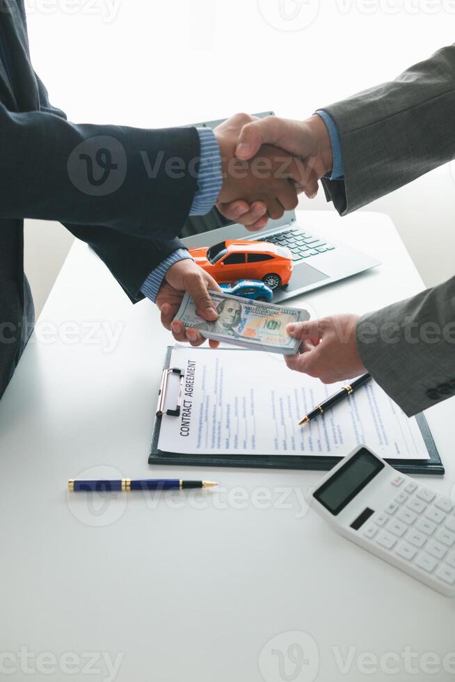 kund och bil -handlare skaka händer efter håller med till försäljning kontrakt innan framställning kontrakt betalning och lämnandet över bil nycklar till kund. begrepp av handslag mellan kunder och bil återförsäljare. foto