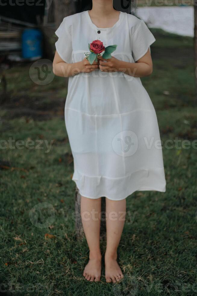 porträtt av en Söt ung kvinna klädd i vit klänning innehav reste sig blommor foto