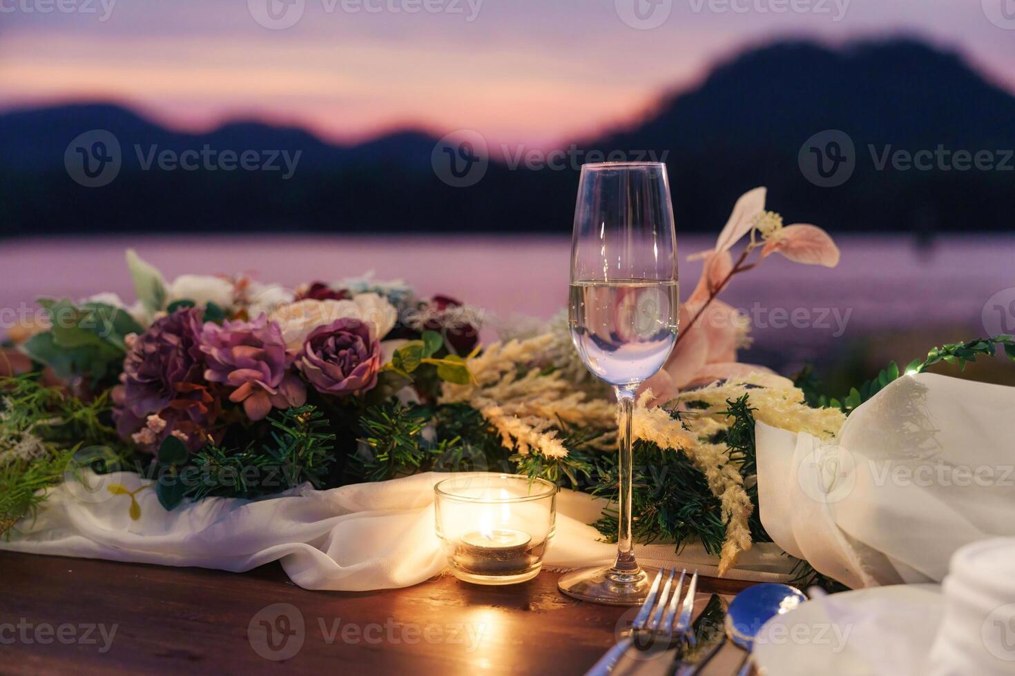 rustik stil dining tabell med blomma, vin glas, ljus dekoration på middag förbi de flod i de solnedgång foto