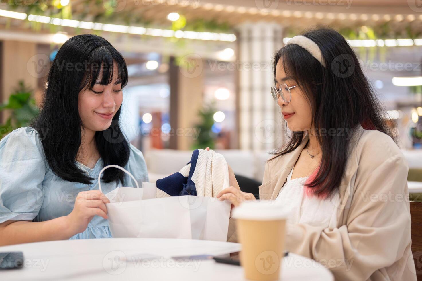 två ung asiatisk kvinnor sitta i en Kafé på en handla köpcenter, granskning kläder de har köpt. foto