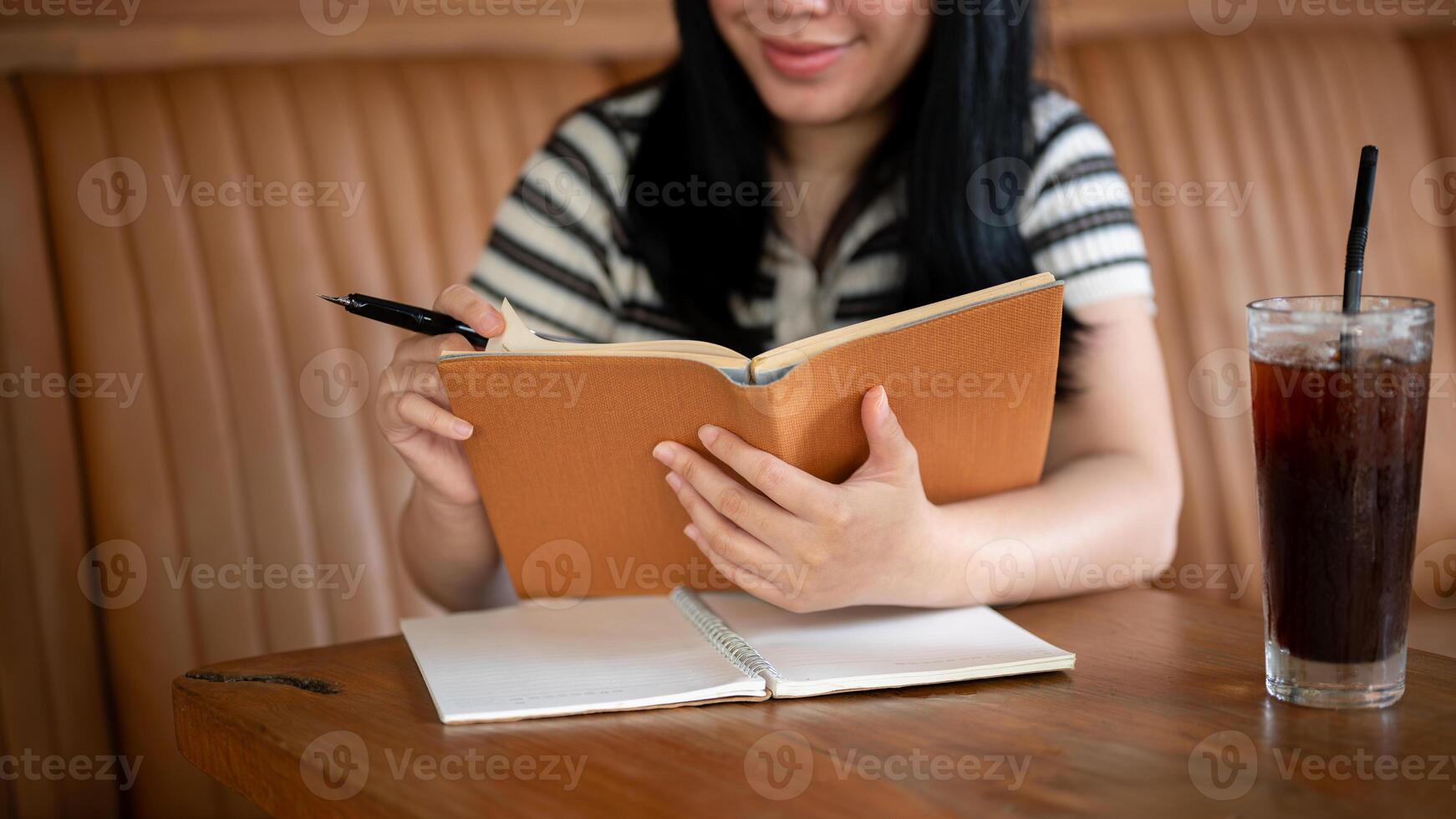 en ung asiatisk kvinna är läsning en bok eller håller på med läxa i en skön årgång kaffe affär. foto