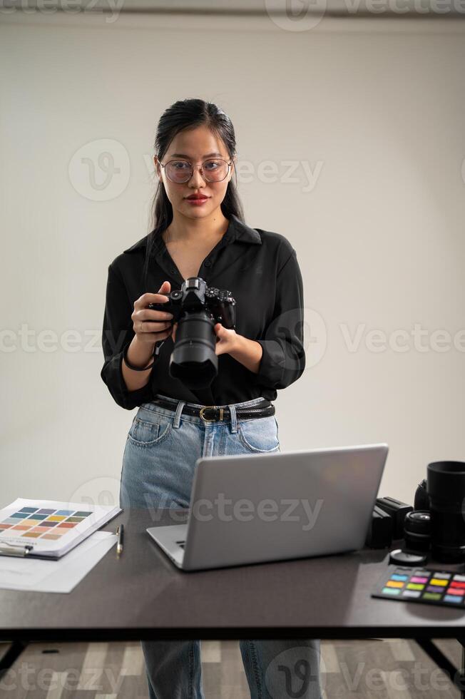 ett elegant asiatisk kvinna fotograf i en svart skjorta med henne dslr kamera är stående i henne studio foto