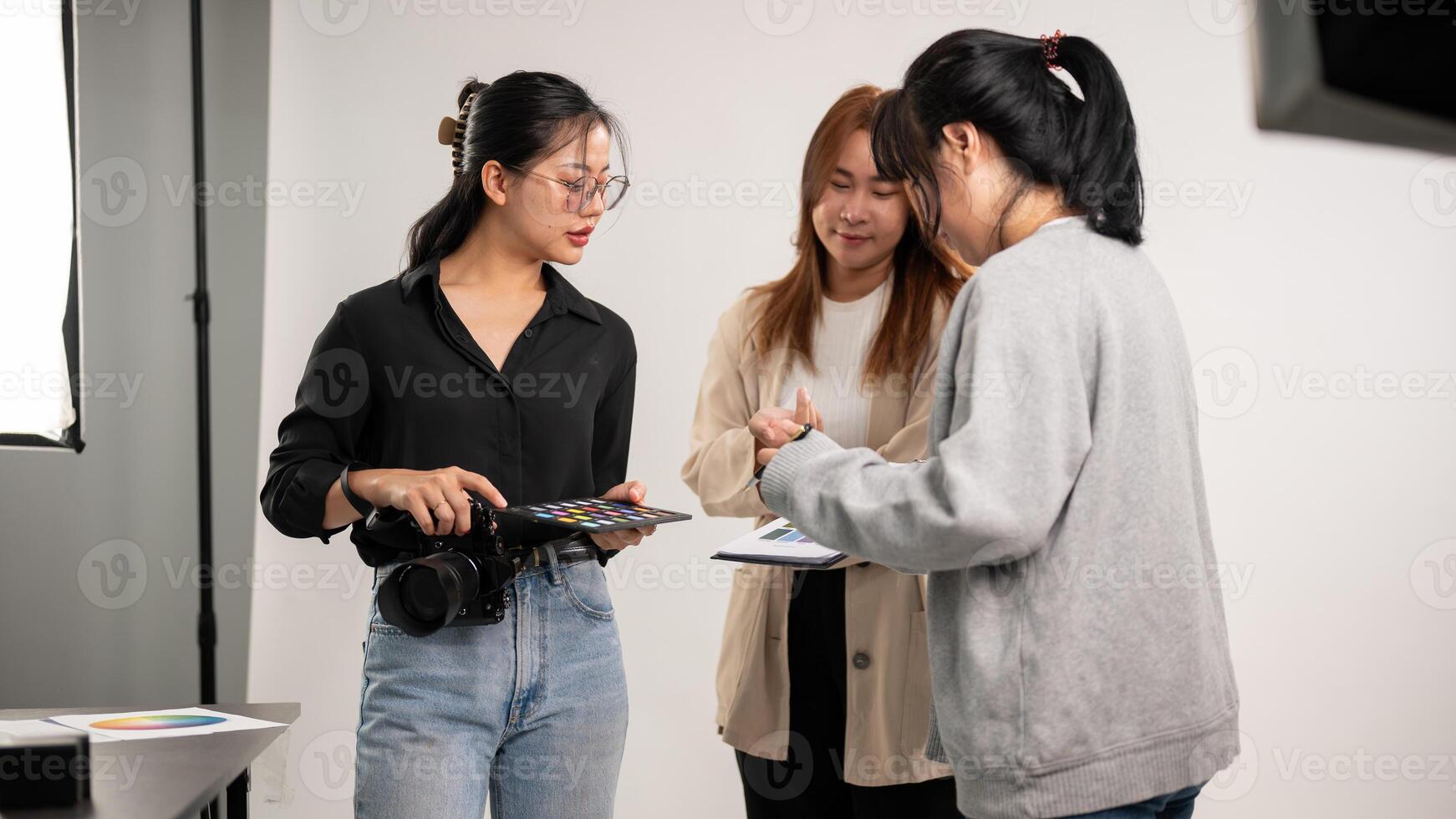 en professionell asiatisk kvinna fotograf talande med assistenter, framställning innan en skytte. foto