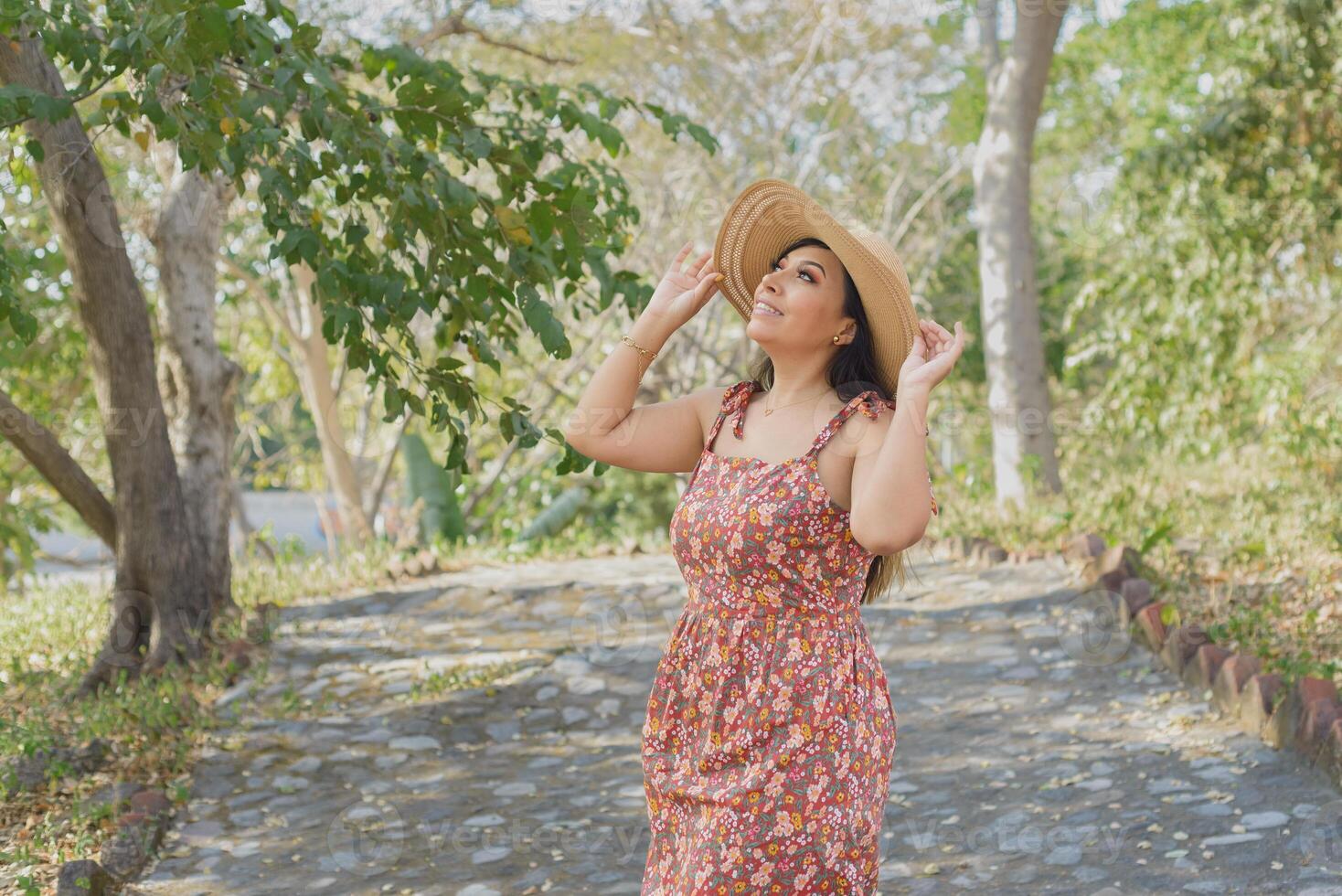 kvinna bär hatt och klänning med blommor beundrande natur i en offentlig parkera. solig sommar dag. foto