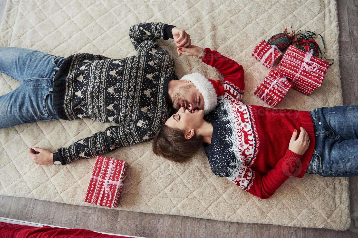 ovanifrån av par i julkläder ligger på golvet med presenter på foto