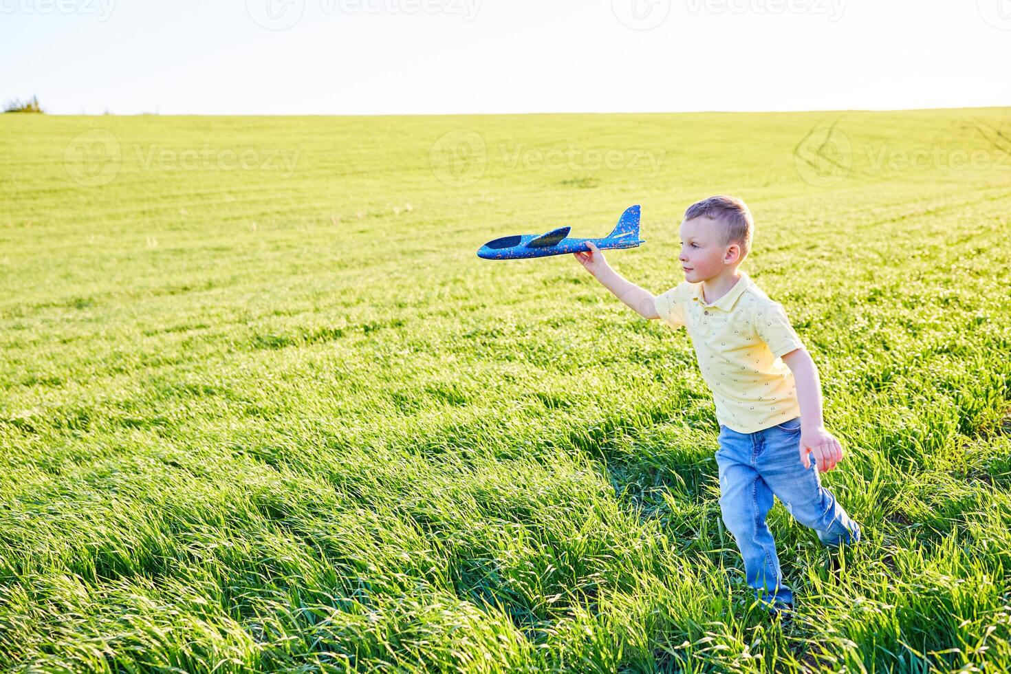 pojke kör med leksak flygplan i sommar genom fält. Lycklig barn löpning och spelar med leksak flygplan utomhus. pojke drömmar av flygande. sorglös barn är spelar. foto