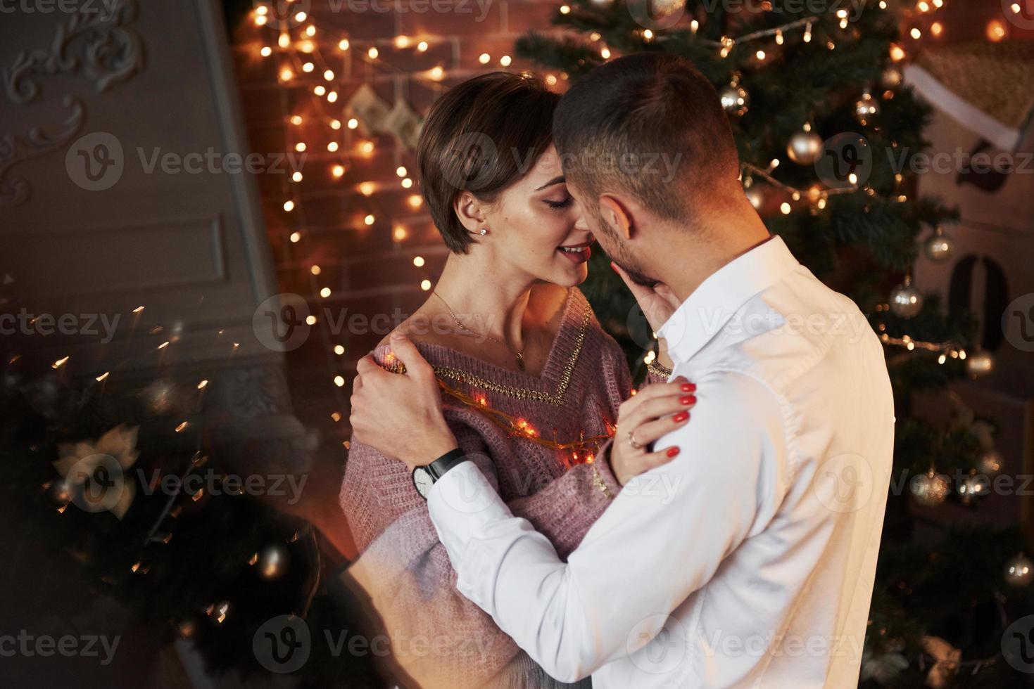reflektion av julgranen. närhet mellan killen och tjejen i lyxkläder som dansar och flirtar foto