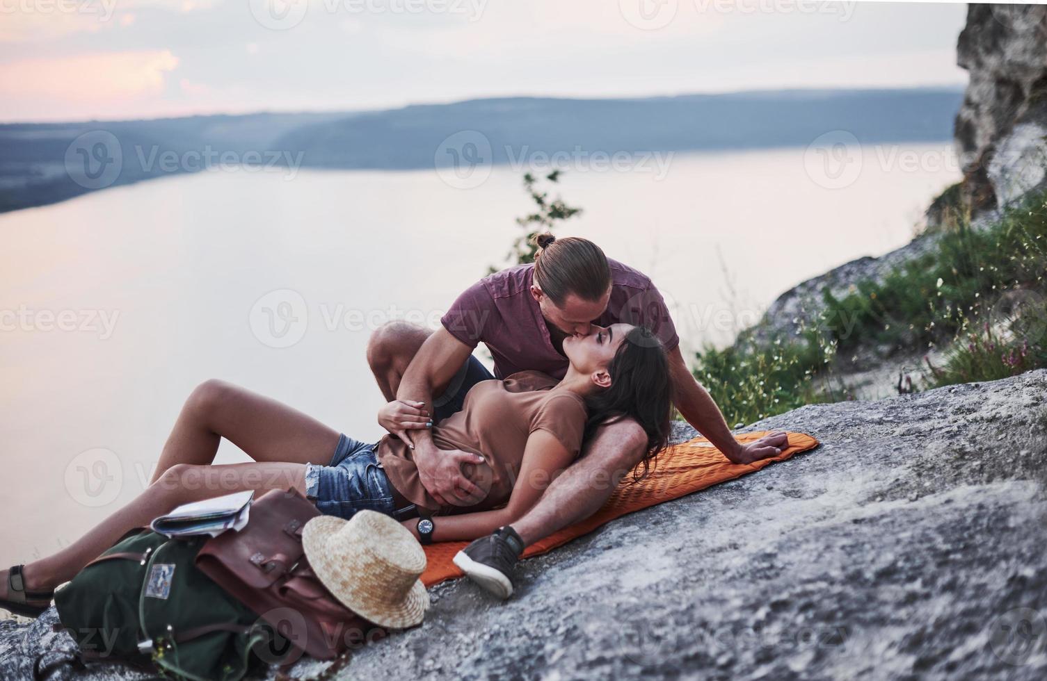 milda känslor. Ungt par har bestämt sig för att tillbringa sin semester på ett aktivt sätt på kanten av den vackra klippan med sjön i bakgrunden foto