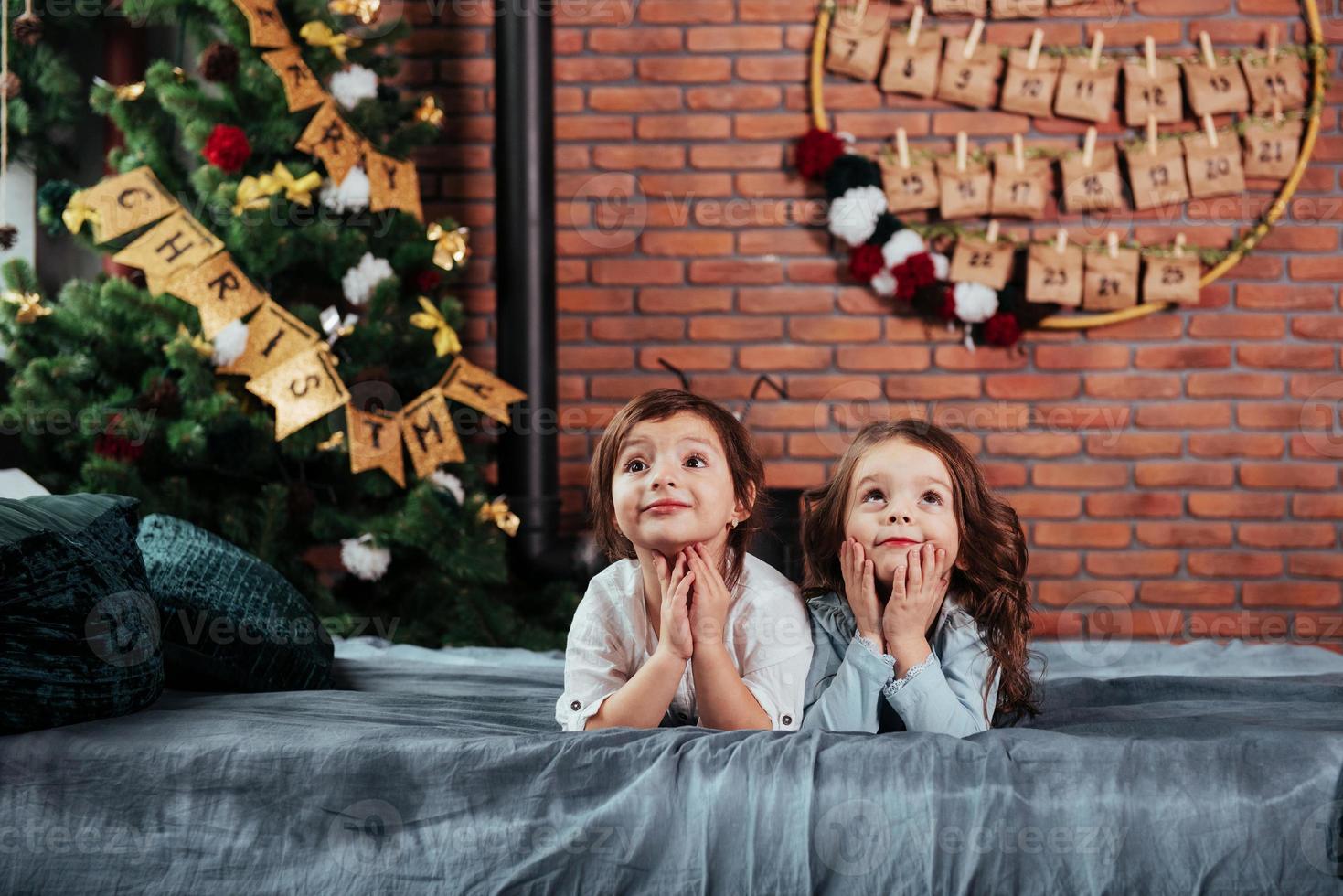 i väntan på gåvor. vad de två glada kvinnliga barn ligger på sängen med nyårsdekorationer och semesterträd foto