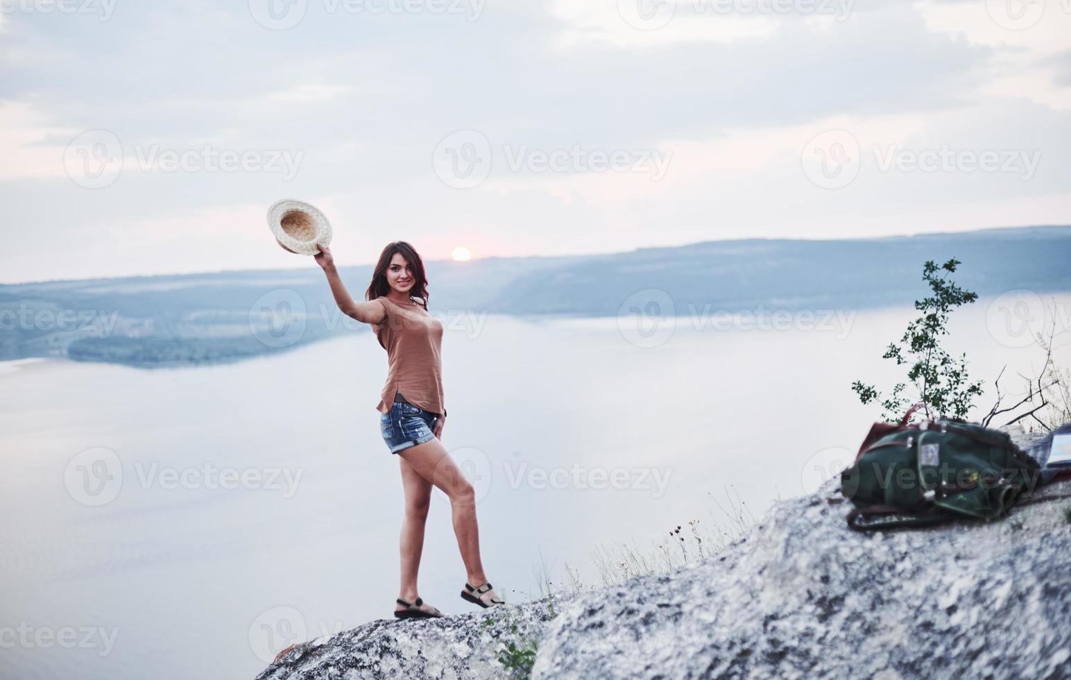 attraktiv turist flicka poserar vid kanten av berget med klart vatten sjön i bakgrunden foto