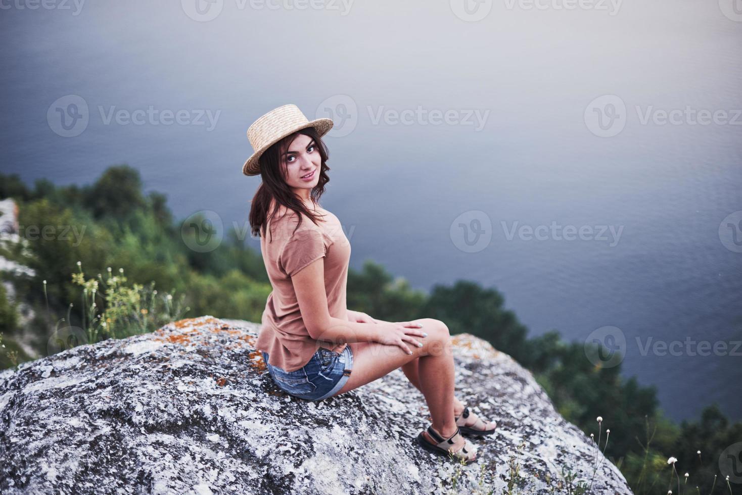 nöjd blick. attraktiv turist flicka poserar vid kanten av berget med klart vatten sjön i bakgrunden foto