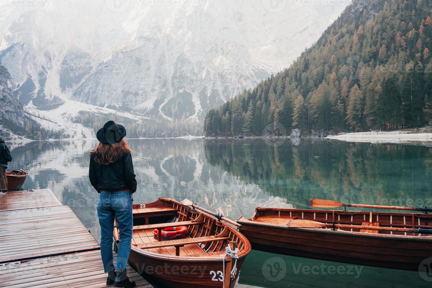 turistisk uppfattning. kvinna i svart hatt njuter av majestätiska bergslandskap nära sjön med båtar foto