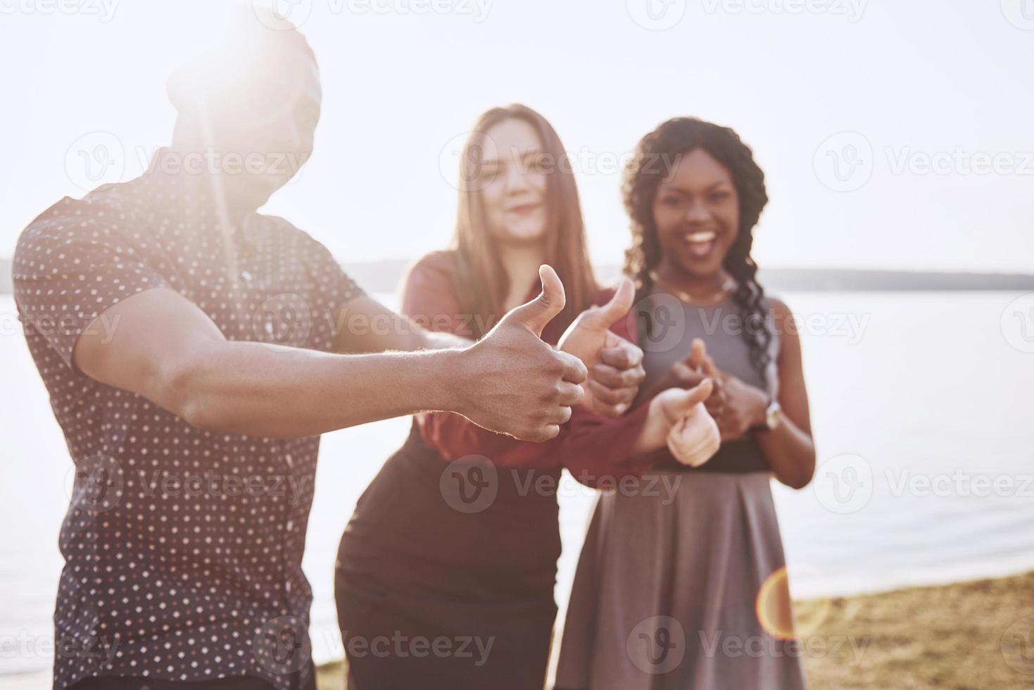 grupp vänner som har roligt utomhus tillsammans. människor kopplar av och chattar i parken vid sjöns strand foto